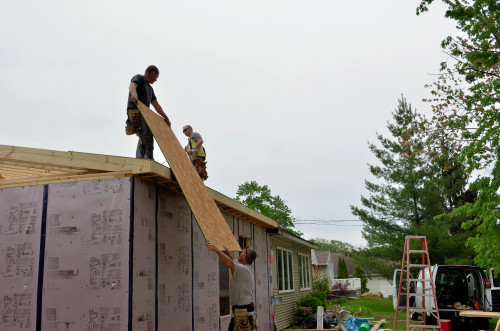 Sheets of roof sheathing are manhandled into place.
